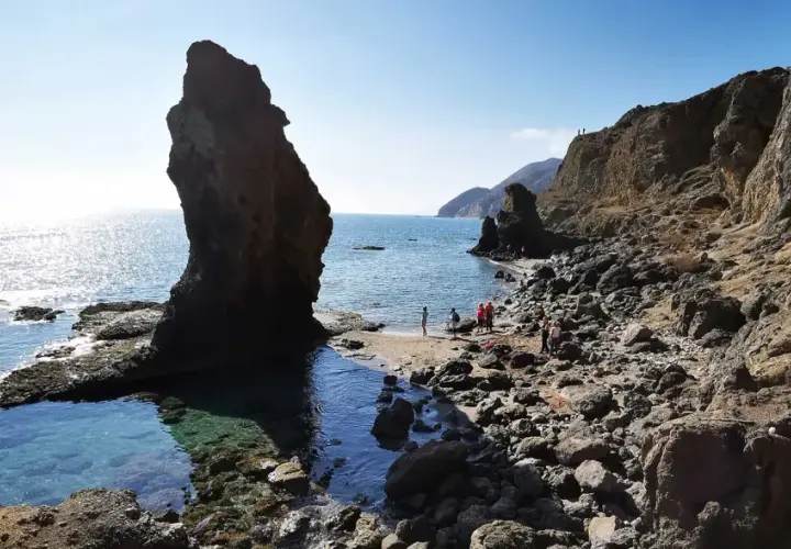 Gente disfrutando de la **playa del Sombrerico**, con sus rocas y aguas cristalinas. ¡Un lugar para guardar en la memoria!