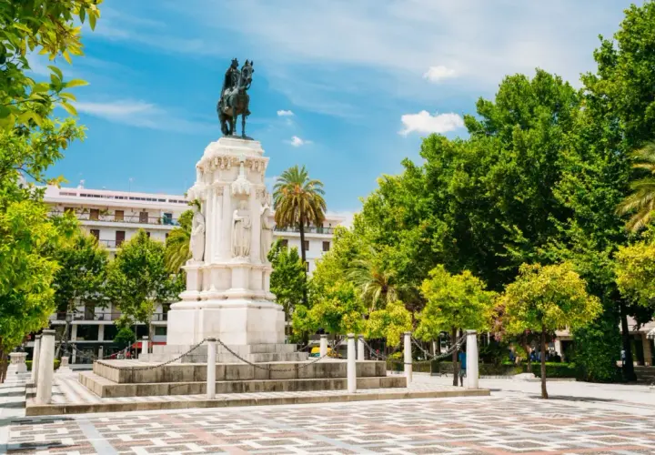 Majestuoso monumento ecuestre, una de las **estatuas en Sevilla**, rodeado de árboles frondosos y un cielo azul vibrante.