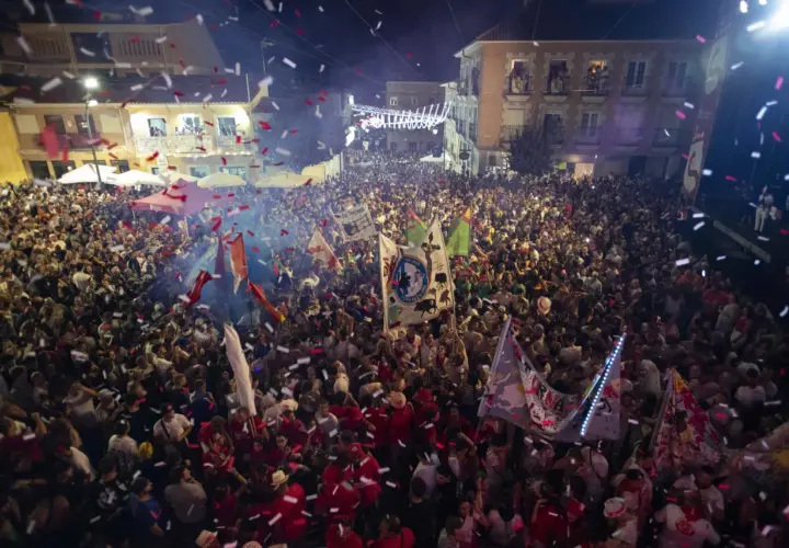 Multitud celebrando con confeti y banderas en una calle por la noche.