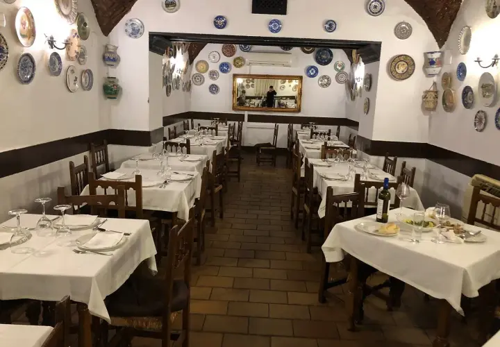 Mesas puestas en el restaurante La Troya Trujillo, decorado con platos de cerámica en las paredes.