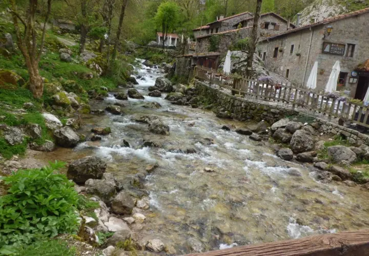 Río caudaloso y rocoso fluye hacia un pueblo de piedra con un cartel que dice "Bar Bulnes Comidas". ¡Así se llega a Bulnes!