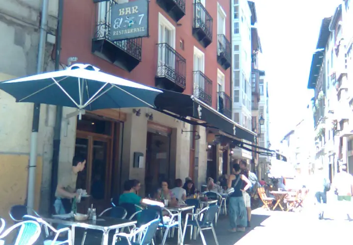 Gente disfrutando en las mesas exteriores del restaurante El 7 Vitoria, bajo un gran parasol azul.