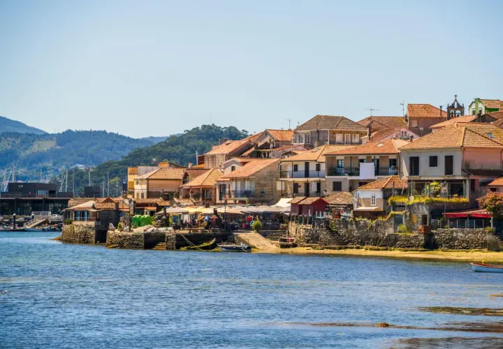 Pueblos de las Rías Baixas con casas de tejados naranjas junto al mar azul, un día soleado.