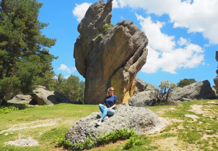 Una mujer sonríe sentada en una roca en un paisaje rocoso y verde. ¡Un lugar increíble que ver en Soria!