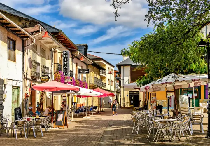 Calle con terrazas de restaurantes en pueblos cerca de León. Hostal La Gallega y Coca-Cola visibles.
