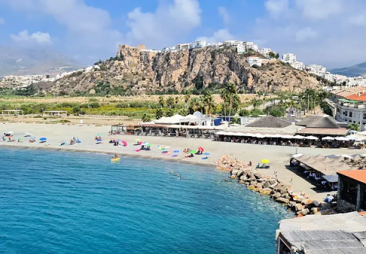 Vista de las playas de Salobreña con gente disfrutando del sol y el mar. El castillo de Salobreña corona la colina.