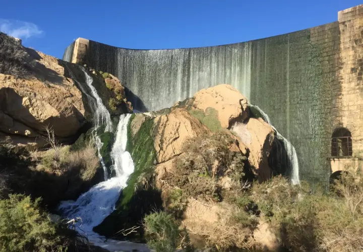 Cascada en la presa de Elche, un lugar ideal para una ruta pantano elche. El agua cae sobre rocas cubiertas de musgo y vegetación.