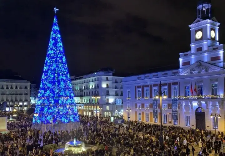 Gran árbol de Navidad azul ilumina la Puerta del Sol, llena de gente, ideal para planes de Navidad en Madrid.