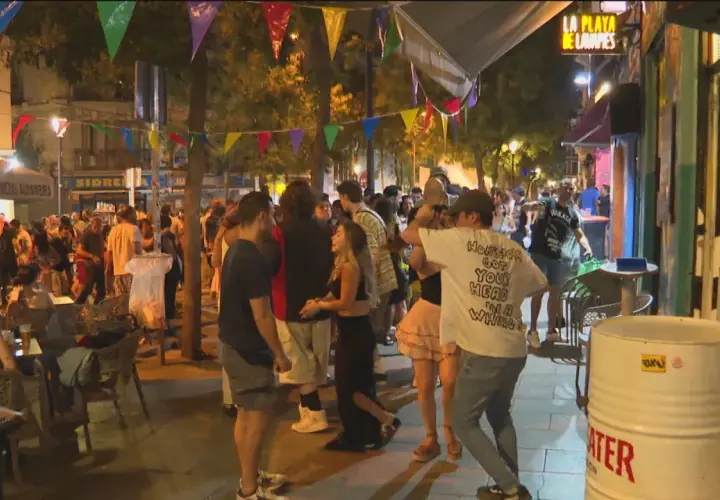 Gente disfrutando de las fiestas de San Lorenzo en Madrid, con luces, música y ambiente festivo en la calle.