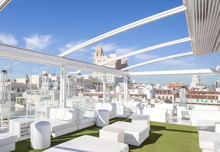 La terraza de Oscar, un oasis blanco con sofás modulares y césped artificial, ofrece vistas urbanas bajo un cielo azul.