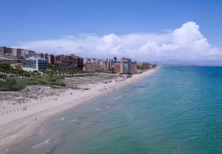 Vista aérea de la playa los Arenales con edificios residenciales al fondo y el mar turquesa.