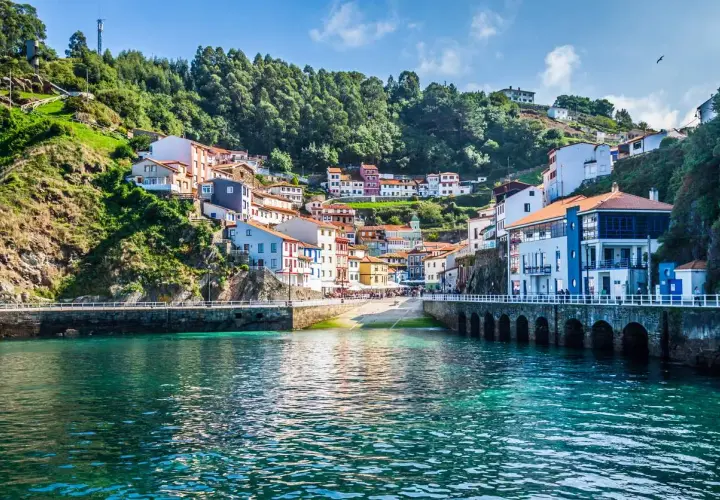 Pueblo costero con casas de colores en una ladera verde, un puerto y aguas turquesas. Un ejemplo de los lugares más bonitos de España.
