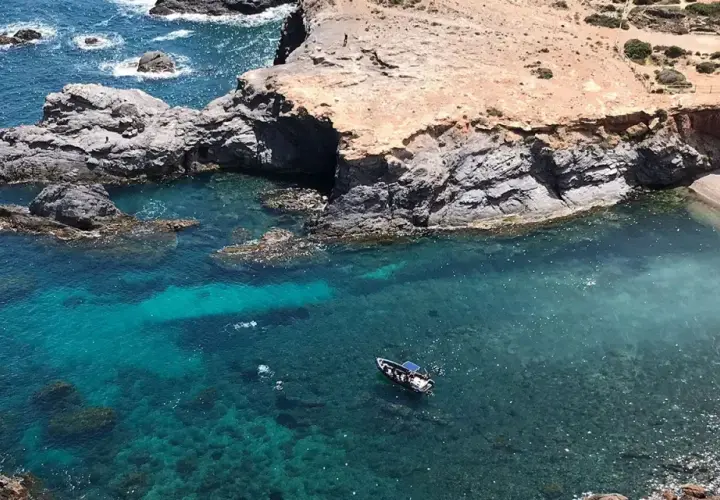 La cala Medina en Cabo de Palos, con aguas cristalinas y una pequeña embarcación, invita a explorar sus secretos.
