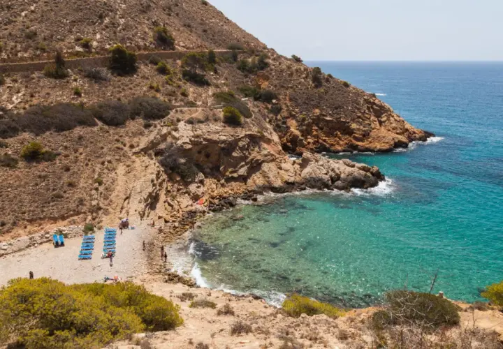 La cala Tío Ximo, con sus aguas turquesas y rocas doradas, invita a relajarse bajo el sol.