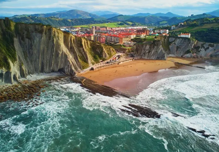 Impresionantes paisajes del País Vasco: acantilados, playa dorada y el mar Cantábrico rompiendo en rocas.