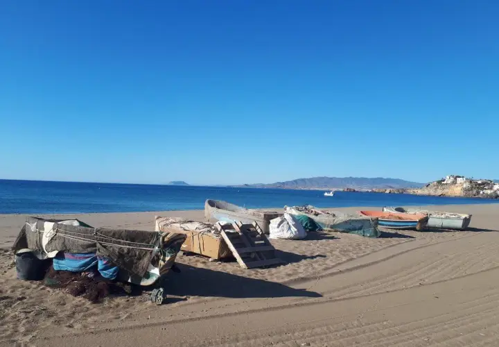 Barcas de pesca cubiertas en la arena de las playas de Mazarrón, con el mar azul y montañas al fondo.