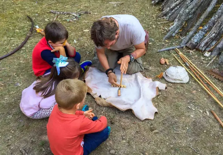 Un hombre enseña a niños a hacer fuego con un arco y un trozo de cuero. ¡Una aventura en la naturaleza para los más pequeños!