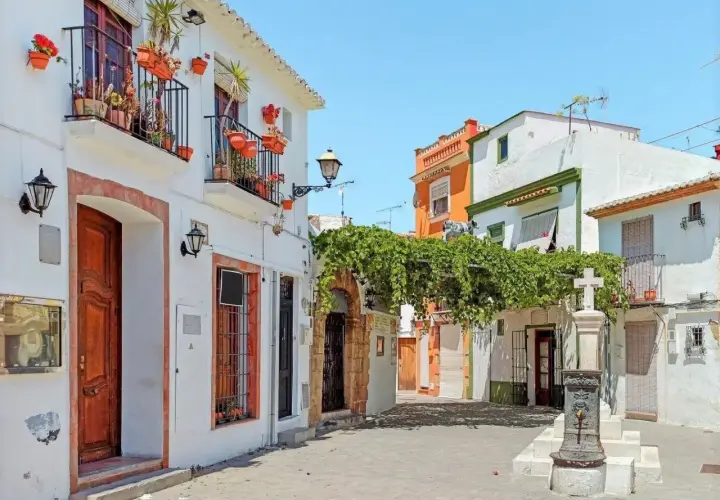 Callejuela con casas blancas, balcones floridos y una fuente. Así es donde está Denia, un rincón con encanto.