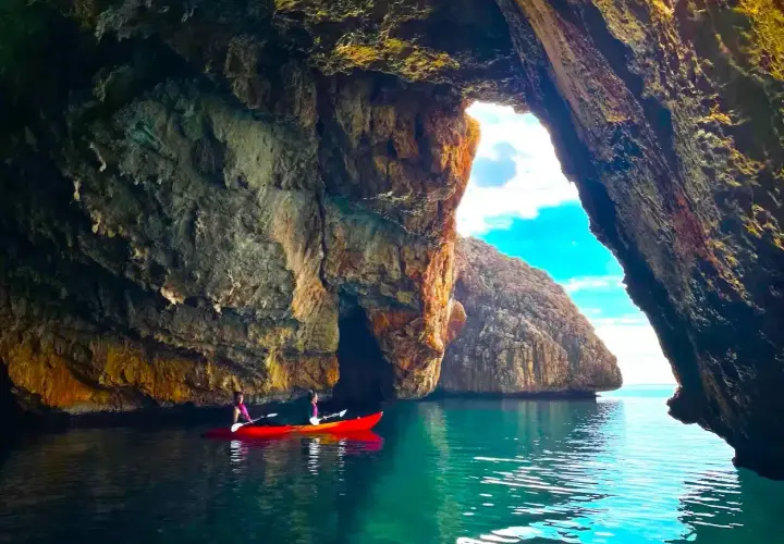 Dos personas en kayak exploran la Cova del Llop Mari en Jávea, con aguas turquesas y formaciones rocosas impresionantes.