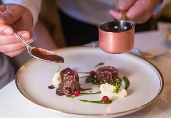 Chef decora un plato de carne con salsa en la granja Madrid.