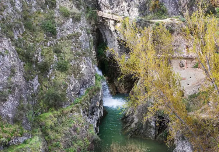 Cascada y ruinas en un cañón. Para saber benilloba como llegar, sigue el sendero entre las rocas y la vegetación otoñal.