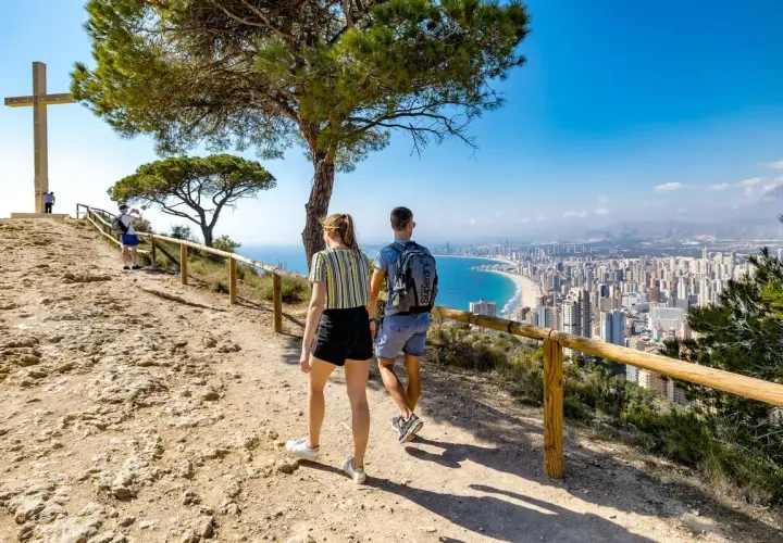 Pareja camina hacia la Cruz de Benidorm, con vistas a la ciudad y la playa.