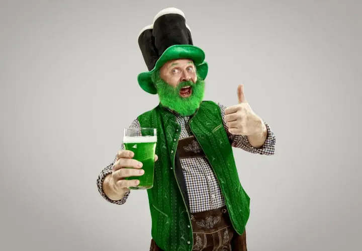 Hombre con barba verde y sombrero de duende, sosteniendo una cerveza verde y dando pulgar arriba. ¡Listo para el desfile de San Patricio!
