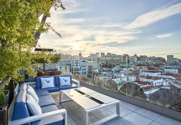 Terraza del Ginkgo restaurante & sky bar con vistas a la ciudad al atardecer. Sofás azules y mesa de centro.
