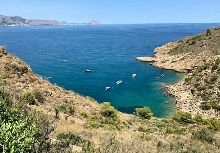 Vista panorámica de la cala de la mina, con aguas turquesas y barcos navegando.