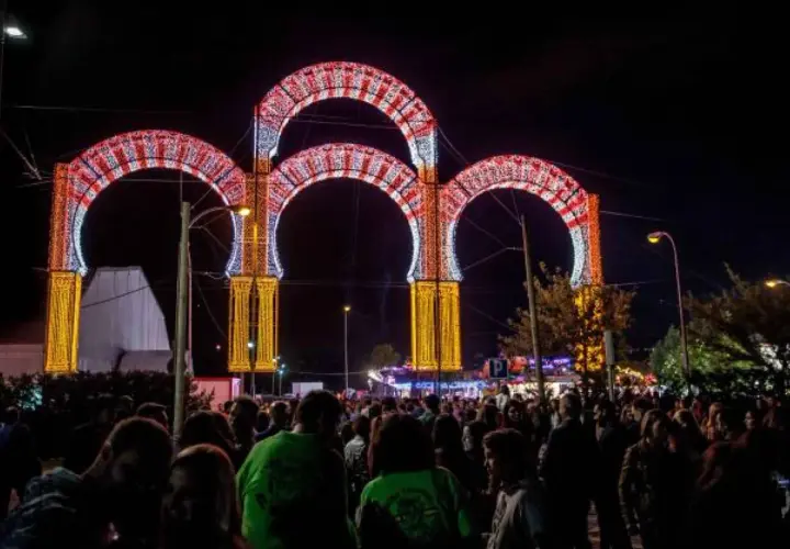 Noche de luces y alegría en las fiestas de Boadilla del Monte. Arcos luminosos decoran la entrada a un evento multitudinario.
