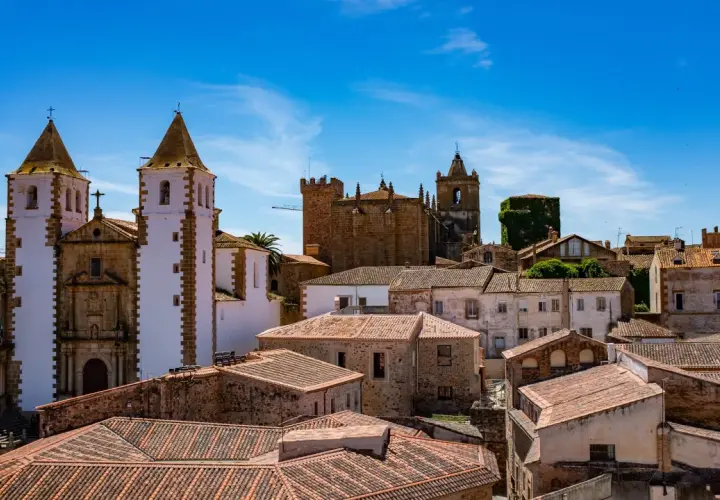 Vistas de tejados y edificios históricos, incluyendo iglesias con torres blancas y campanarios, bajo un cielo azul. Un lugar ideal que ver en Cáceres provincia.