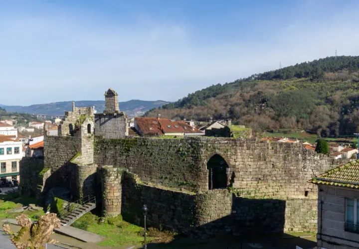Ruinas de un castillo de piedra, con tejados rojos y colinas verdes al fondo. Un ejemplo de los pueblos bonitos cerca de Monforte de Lemos.