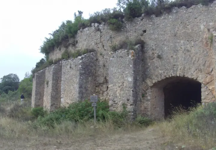 Antigua construcción de piedra en la Serra de Mariola, con un arco de entrada y vegetación circundante.