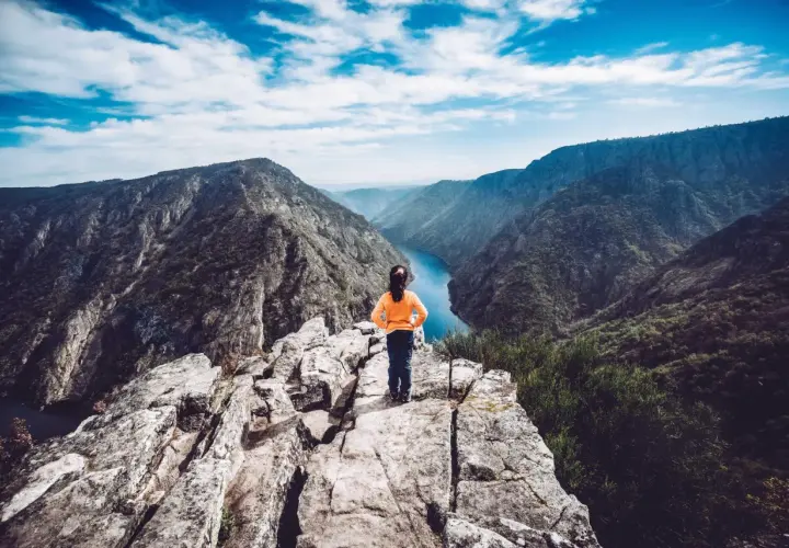 Niña en el mirador de Vilouxe, contemplando un cañón con un río azul y montañas verdes bajo un cielo nublado.
