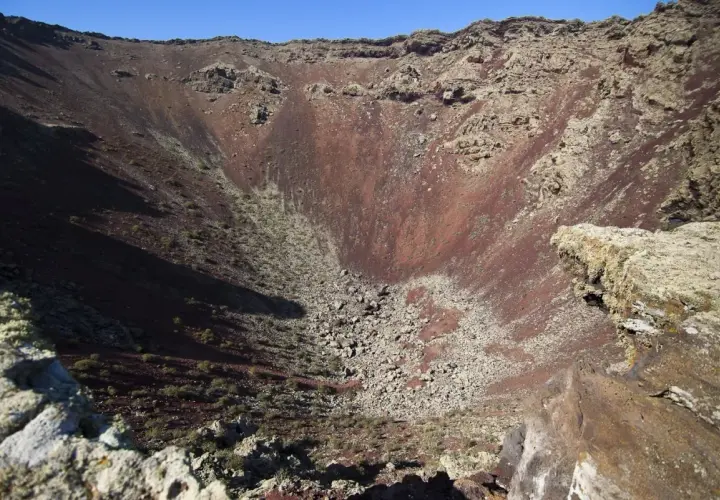 Interior del cráter del Volcán de la Corona, con rocas rojizas y vegetación escasa.