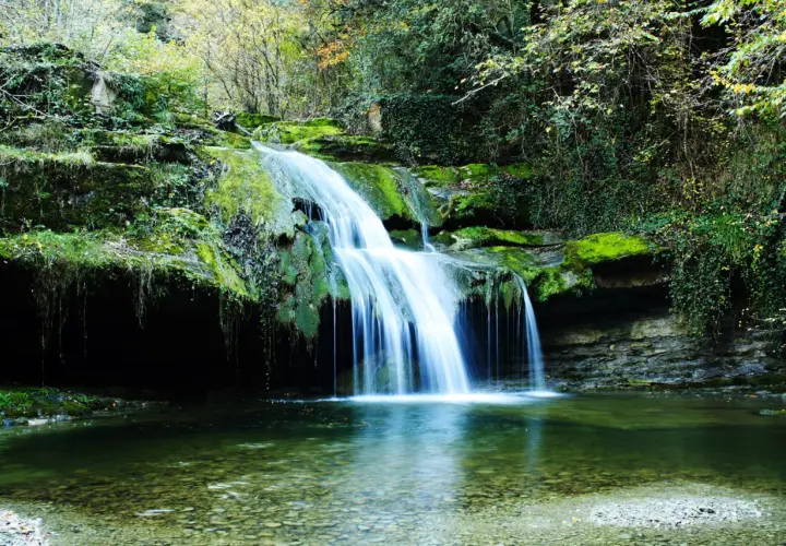 Cascada en un bosque frondoso, un rincón idílico de los parques naturales de España. El agua cae sobre rocas cubiertas de musgo, creando un espectáculo natural.