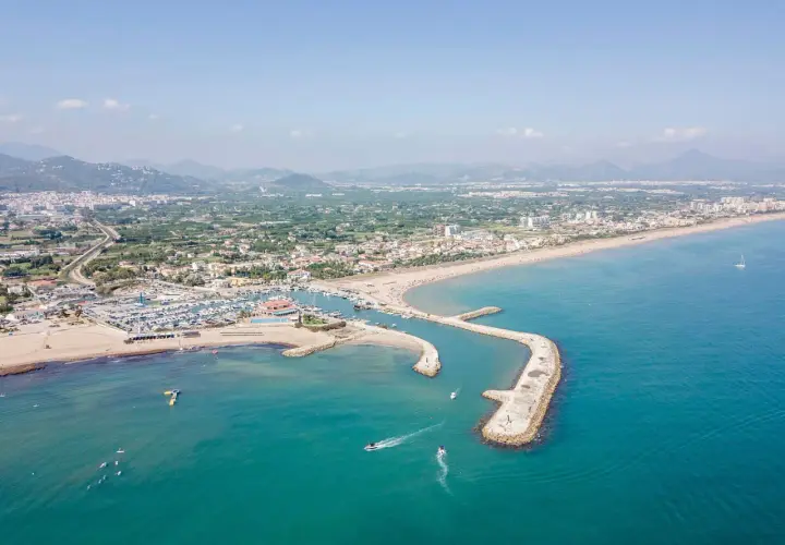 Vista aérea de la playa de Oliva, con su puerto deportivo, arena dorada y aguas turquesas. Las opiniones sobre la playa de Oliva son muy positivas.