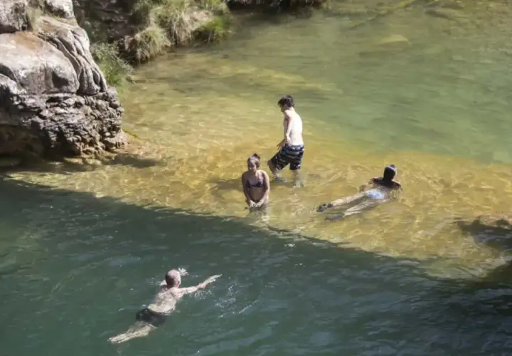 Gente disfrutando de un día en las playas cerca de Zaragoza, nadando y refrescándose en aguas cristalinas.