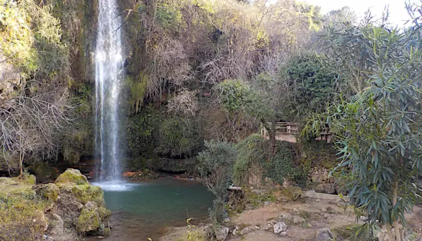 Los chorradores de Navarres, una cascada cae en una poza de agua verde rodeada de vegetación y rocas.