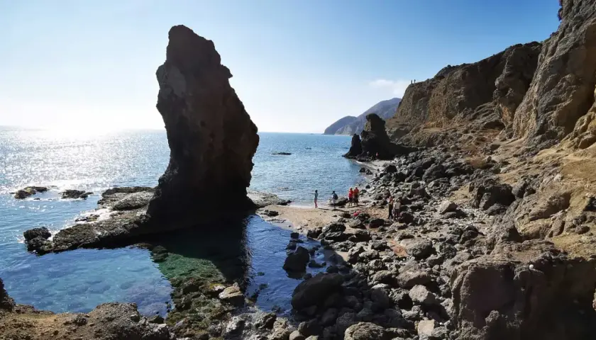 Gente disfrutando de la **playa del Sombrerico**, con sus rocas y aguas cristalinas. ¡Un lugar para guardar en la memoria!