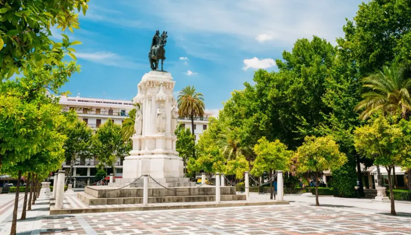Majestuoso monumento ecuestre, una de las **estatuas en Sevilla**, rodeado de árboles frondosos y un cielo azul vibrante.