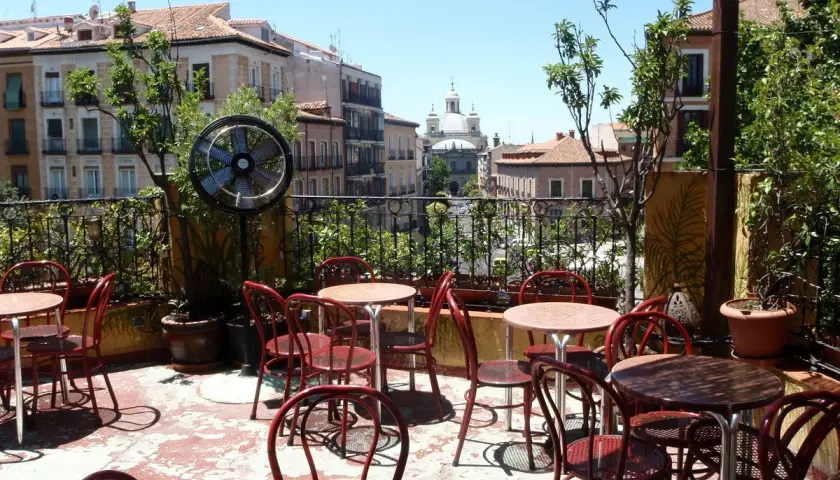 Terraza de verano en Madrid, con mesas y sillas rojas, ventilador y vistas a edificios históricos. Un lugar perfecto para el viajero madrileño.