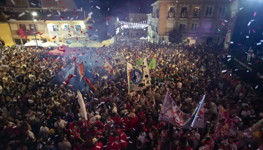 Multitud celebrando con confeti y banderas en una calle por la noche.