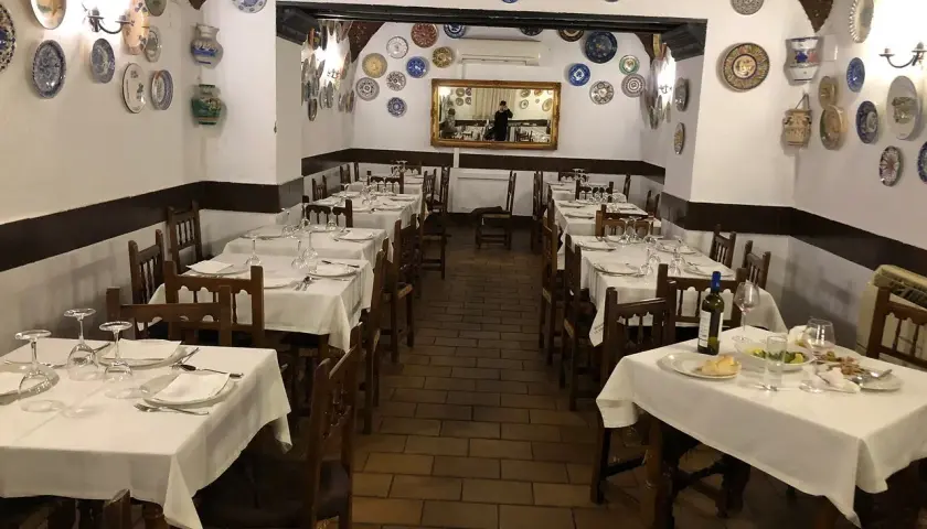 Mesas puestas en el restaurante La Troya Trujillo, decorado con platos de cerámica en las paredes.