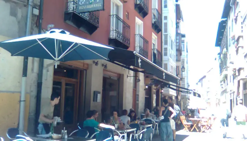 Gente disfrutando en las mesas exteriores del restaurante El 7 Vitoria, bajo un gran parasol azul.
