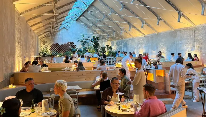 Gente cenando en un moderno espacio tramo Madrid, con techos altos y luz natural.