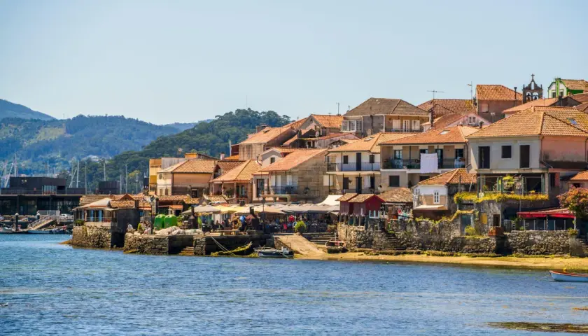 Pueblos de las Rías Baixas con casas de tejados naranjas junto al mar azul, un día soleado.