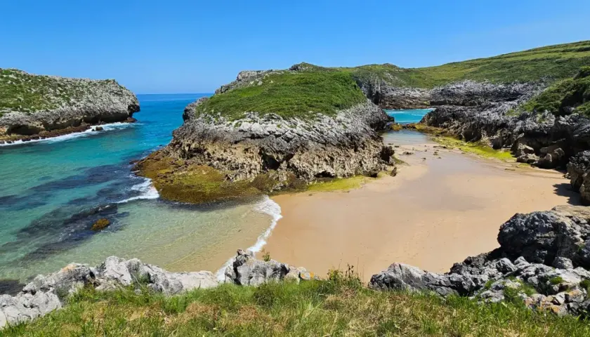 Una cala asturiana con aguas turquesas y arena dorada, rodeada de acantilados verdes. Un paraíso entre las playas más bonitas de Asturias.