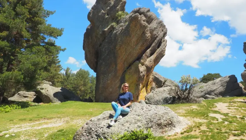 Una mujer sonríe sentada en una roca en un paisaje rocoso y verde. ¡Un lugar increíble que ver en Soria!