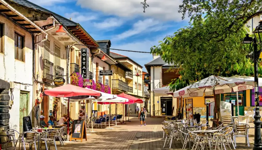 Calle con terrazas de restaurantes en pueblos cerca de León. Hostal La Gallega y Coca-Cola visibles.